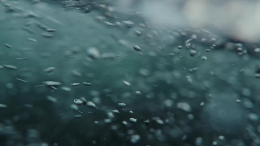 An abstract close-up shot of turbulent water shows countless bubbles swirling around in slow motion