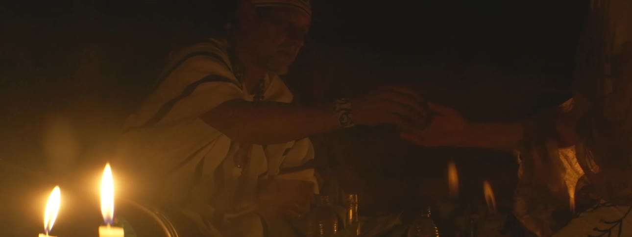 An indigenous shaman conducts a spiritual ceremony by candlelight, carefully preparing and offering a sacred mixture in slow motion
