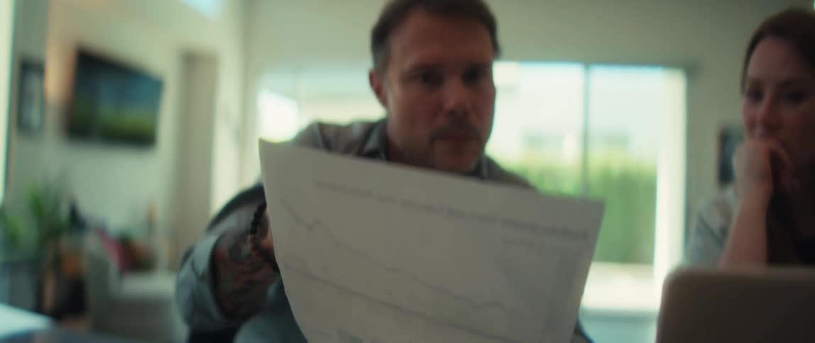 A concerned man with tattoos on his arm reviews a financial chart showing a steep decline in portfolio performance