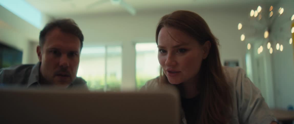 A man and woman sit at a kitchen island in their modern home, seriously reviewing information together on a laptop