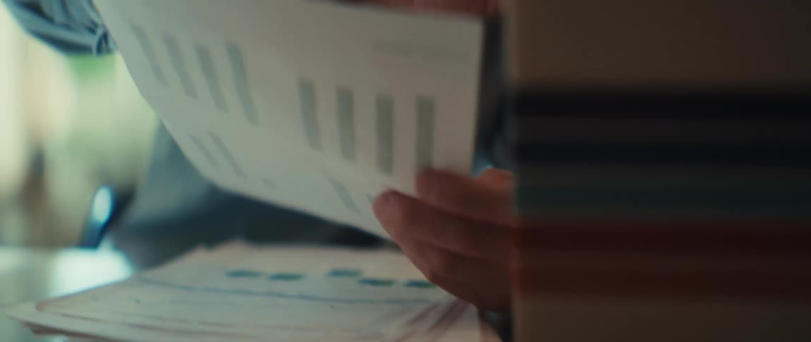A slow pan shot reveals a couple working on their household finances, using a calculator and reviewing charts and graphs at their desk