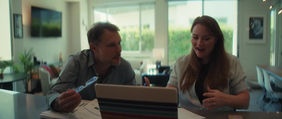A male and female coworker enthusiastically collaborate on a presentation, pointing at a laptop and smiling in a modern workspace