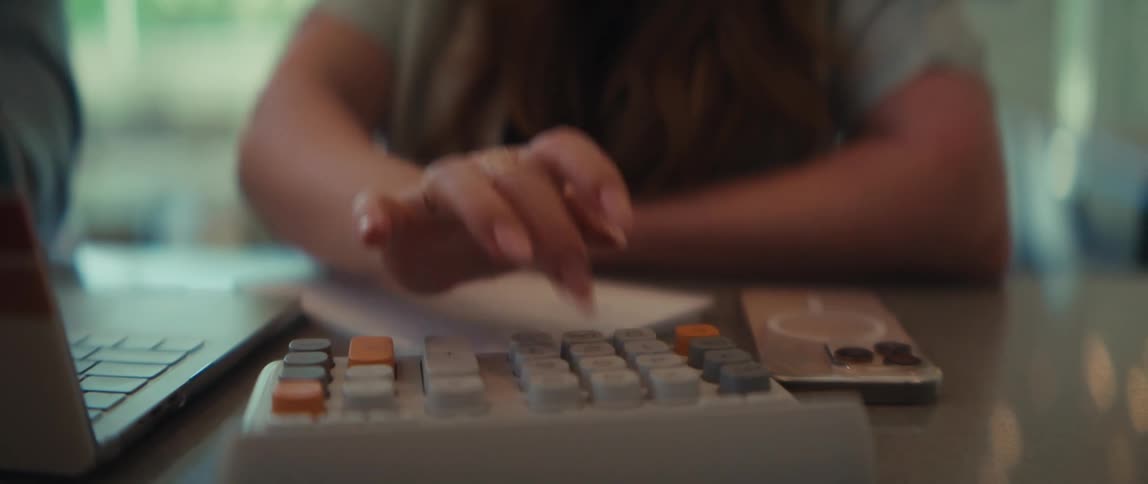 A slow-motion shot pans between colleagues as one analyzes business data on a chart and the other uses a calculator