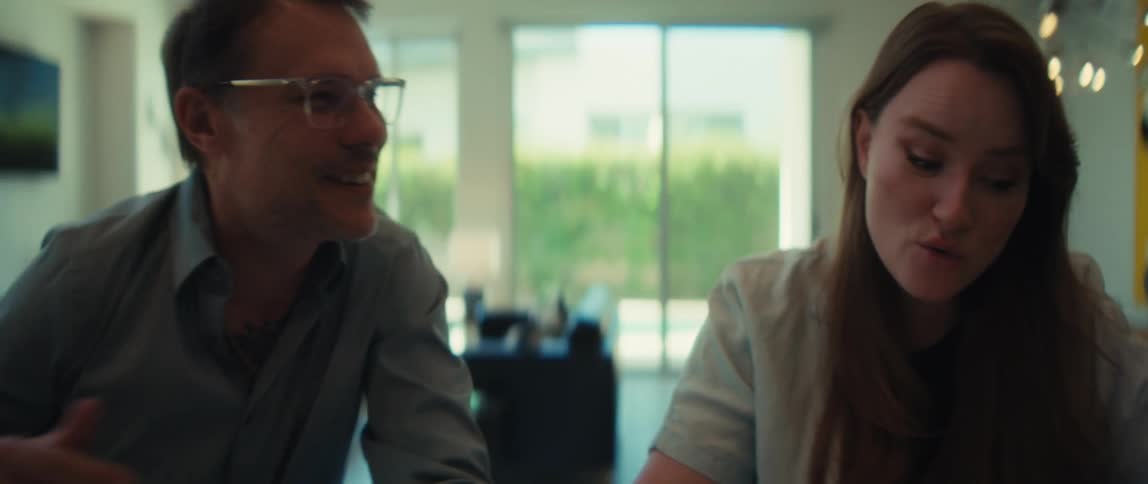 Slow pan from a professional man talking to a woman smiling during a meeting in a modern, naturally lit office