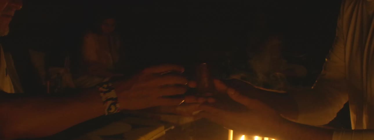 A shaman guides a sacred Ayahuasca ceremony by candlelight, passing a ceremonial drink to a participant in a slow-motion shot