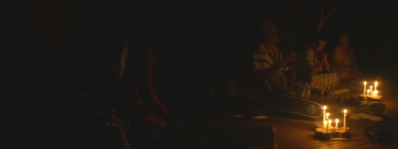 A shaman leads a traditional spiritual ceremony in a dark room illuminated only by candlelight