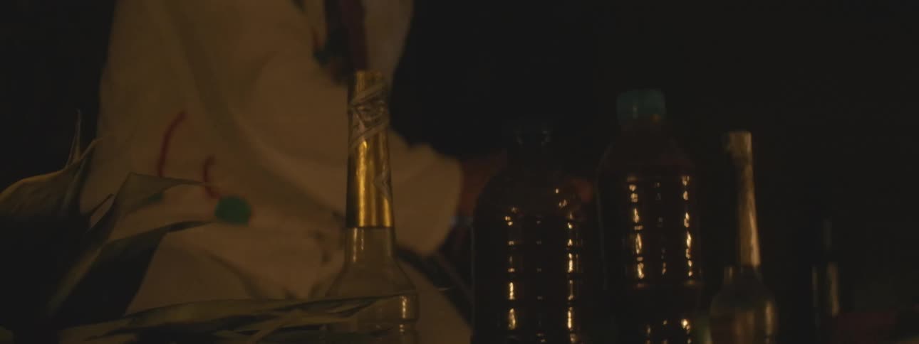 Bottles and leaves are arranged as offerings during a candlelit cultural ceremony at night