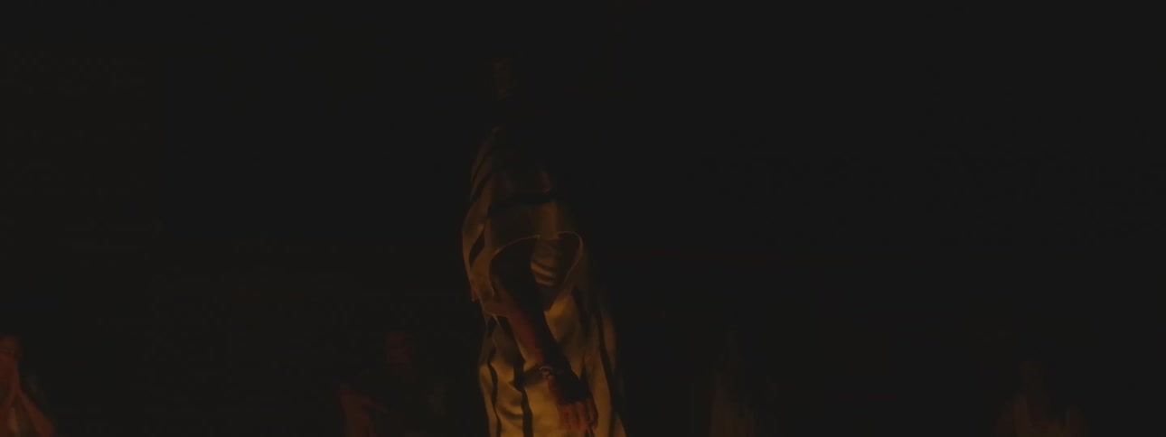 A shaman in traditional clothing conducts a sacred ritual, blessing his followers in the warm glow of a campfire at night