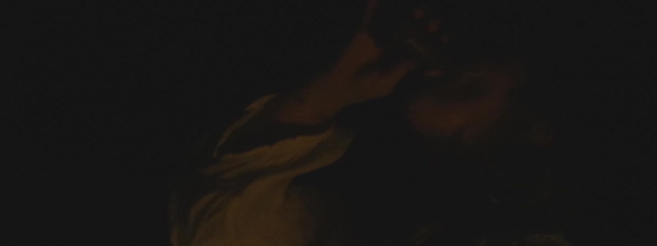 A woman in period clothing receives a rosary from a man during a secret meeting lit by flickering candlelight