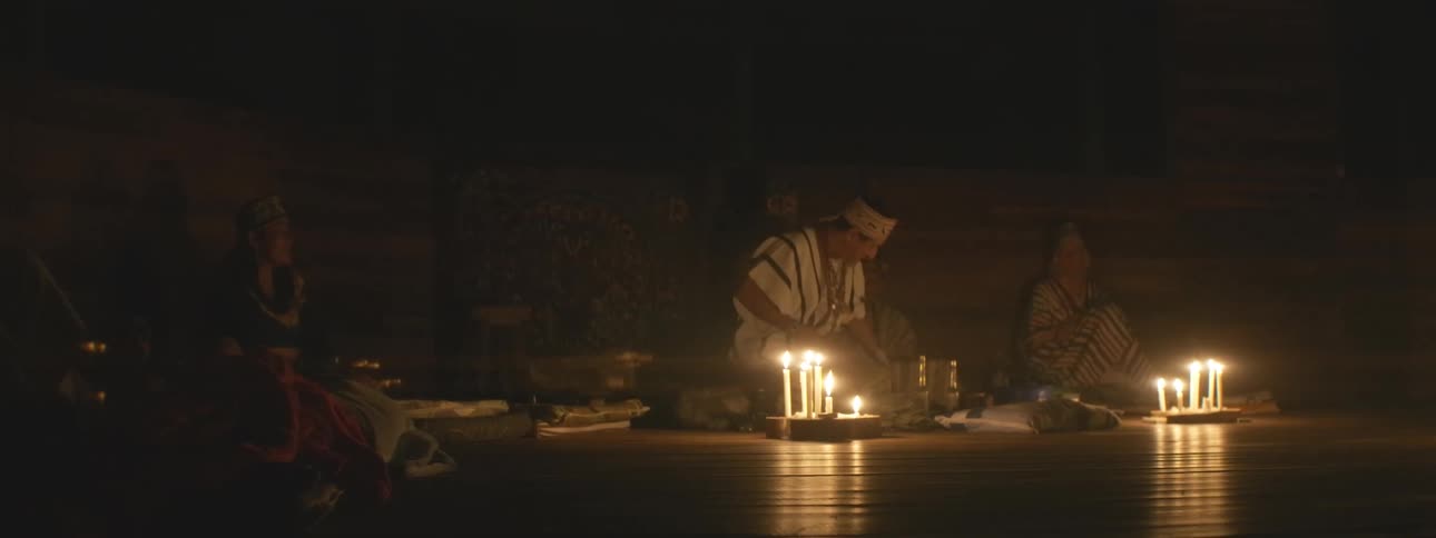 A shaman leads a spiritual ceremony by candlelight in a dark, sacred space