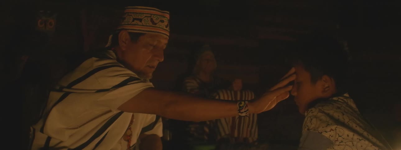 An indigenous shaman in traditional clothing performs a sacred candlelight blessing ceremony on a young boy