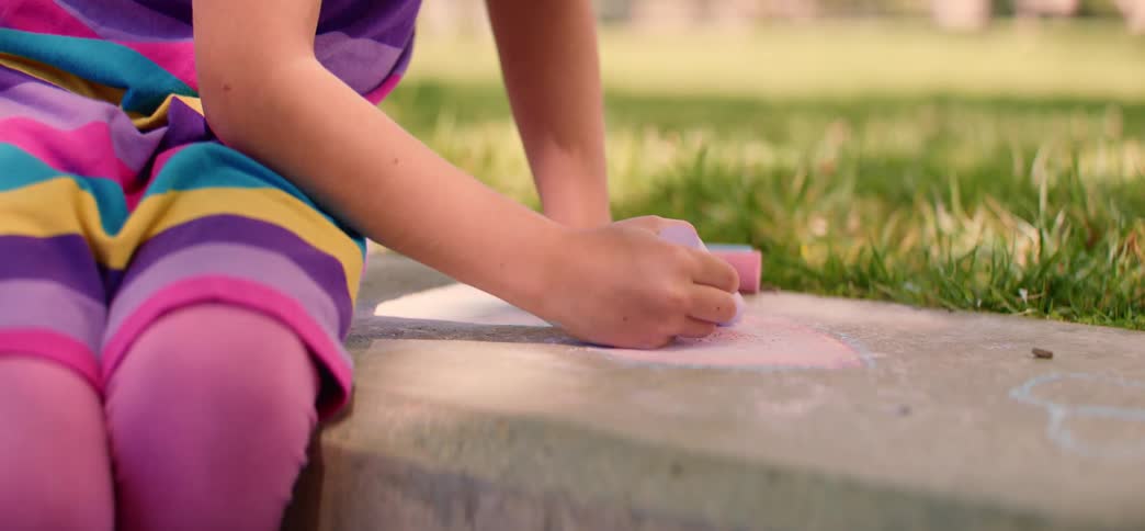 Close up shot of a young girl's hands coloring with sidewalk chalk on a sunny day