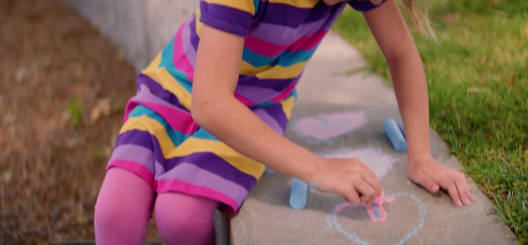 Slow motion tilt reveals a creative young girl drawing colorful hearts with chalk on a concrete curb