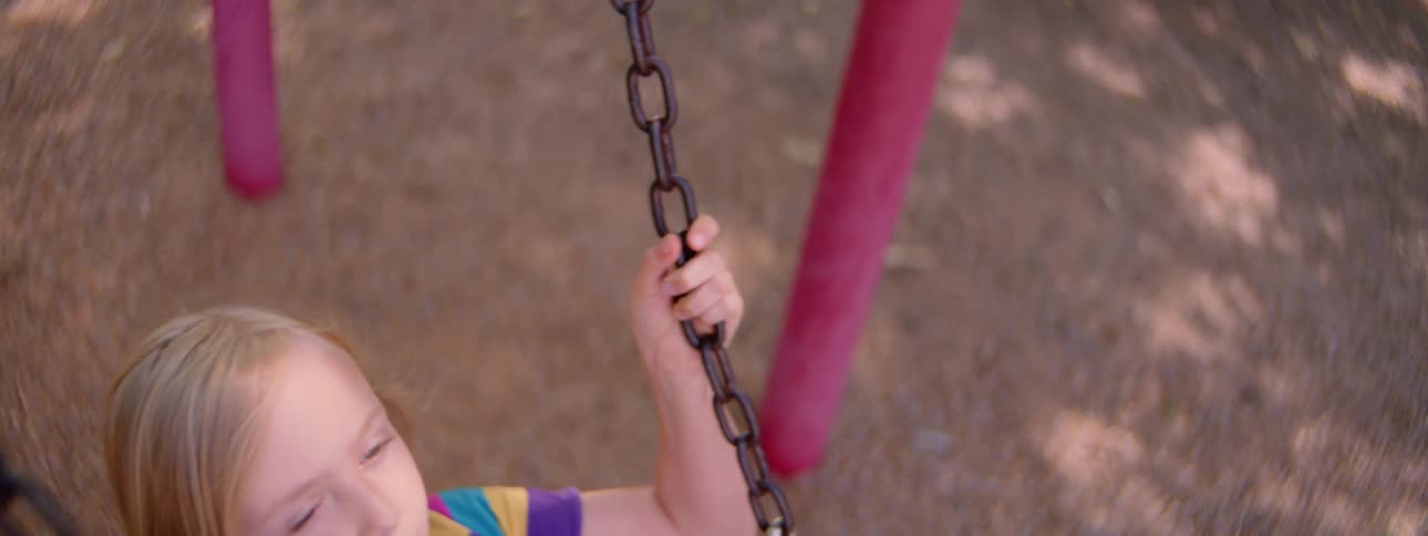 A young girl in a colorful striped dress swings in slow motion on a playground swing set