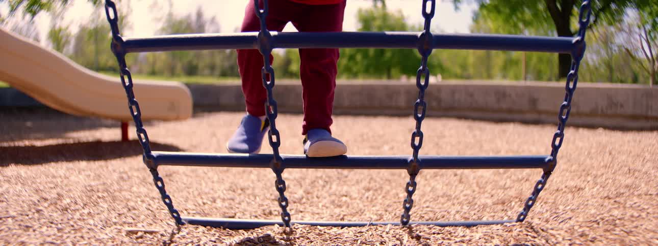 A close-up in slow motion of a child's feet carefully climbing on a wobbly playground structure