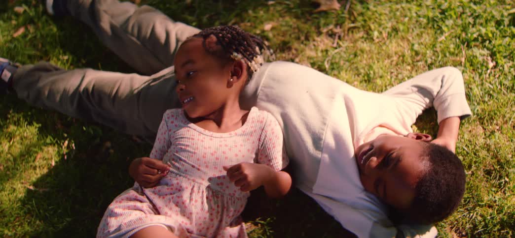 A sweet brother and his little sister relax together in the warm sunlight while lying on the green grass