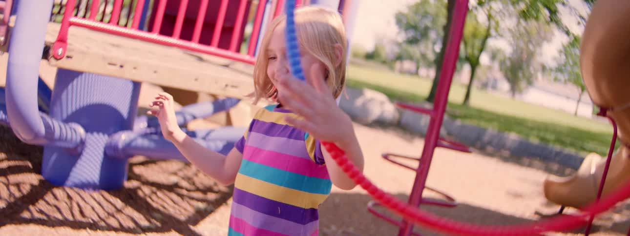 Slow motion shot of a happy little girl spinning a hula hoop on her arm at a playground on a sunny day