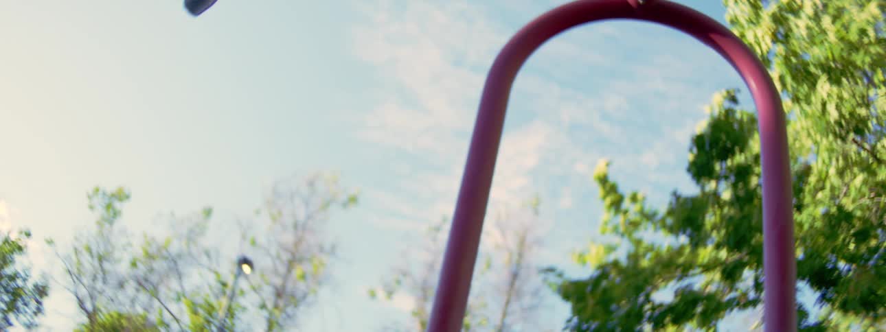 A young boy wearing a backwards cap soars into the sky on a playground swing in slow motion