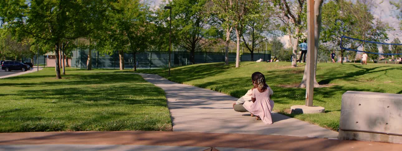Adorable young African American siblings ride together on a skateboard down a path in a sunny park