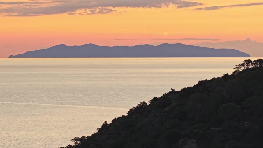 A slow zoom reveals a distant island across a calm sea during a beautiful golden hour sunset