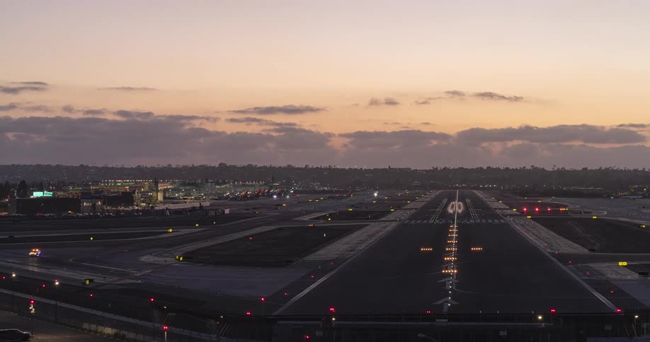 A dynamic day-to-night timelapse captures the bustling activity of planes landing and taxiing on an airport runway as dusk turns into a vibrant night