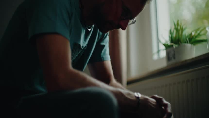 A slow tilt-up reveals a pensive and sorrowful man sitting alone in a dimly lit room