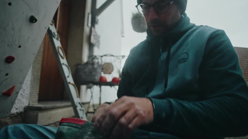 A focused man prepares for rock climbing by chalking his hands from his chalk bag in cinematic slow motion