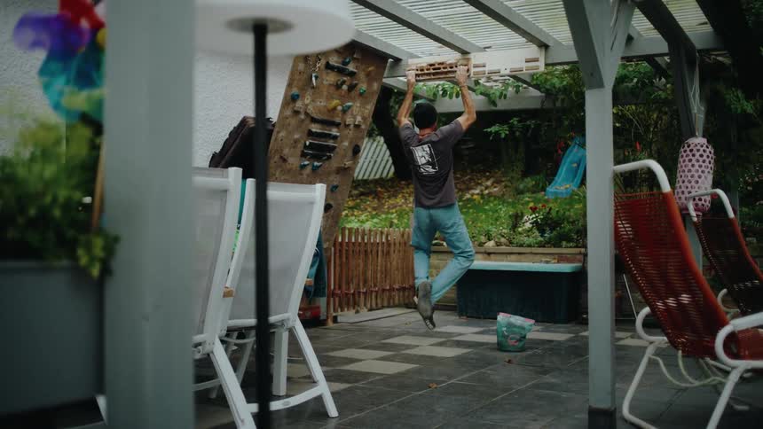 A male climber trains his finger strength on a hangboard in his backyard in slow motion