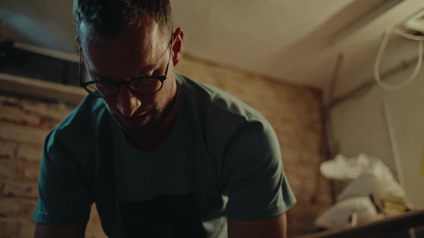 A determined man performs bent-over dumbbell rows in a gritty, dimly lit basement home gym