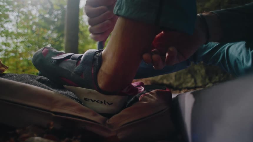 Close-up slow motion shot of a rock climber putting on and tightening their climbing shoe in a sunlit forest