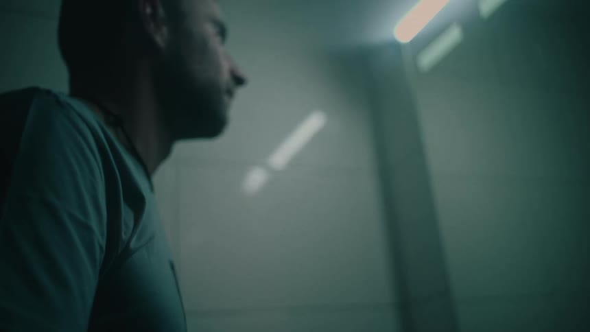 A contemplative man in a dimly lit bathroom dries his face in slow motion before putting on his glasses and looking in the mirror