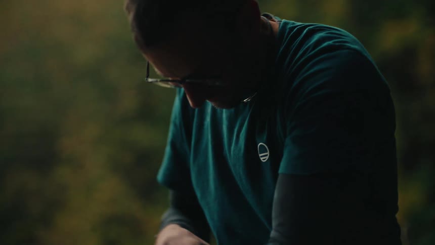 A contemplative man in glasses sits in a moody forest setting, chalking his hands and looking up thoughtfully before his climb