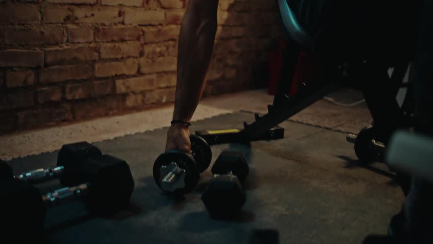 Focused man warms up and performs a dumbbell chest press on a bench in his rustic basement home gym