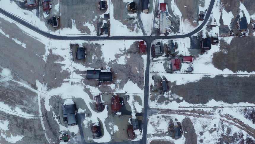 A slow ascending top-down aerial shot reveals a small rural neighborhood covered in patches of snow during winter