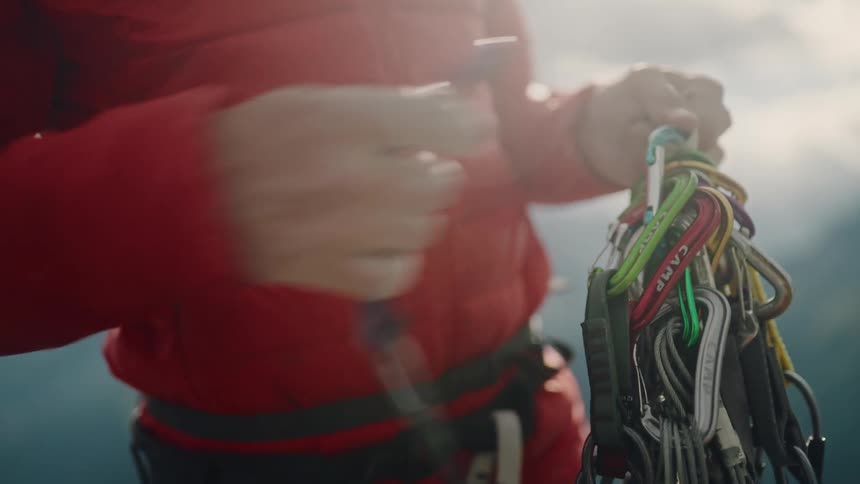 A climber meticulously sorts colorful quickdraws and clips them onto their harness in preparation for a mountain ascent