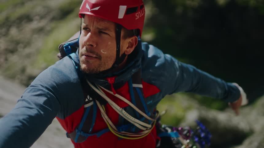 A male rock climber in a red helmet concentrates as he chalks his hand for the next grip in slow motion