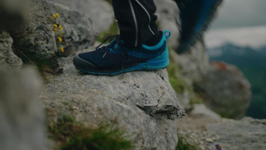 Close-up slow-motion shot of a hiker's feet in athletic shoes carefully ascending a rocky mountain trail