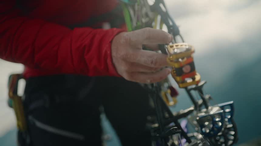 A rock climber carefully selects a piece of traditional climbing gear from their harness in slow motion