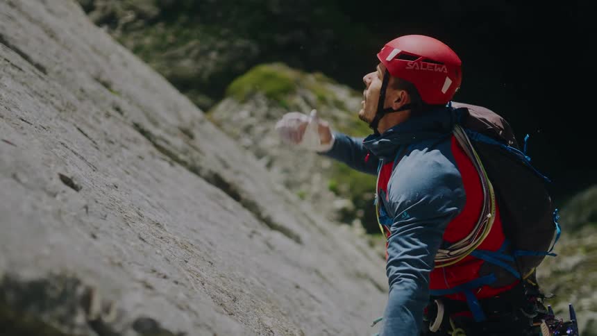 An alpinist chalks his hands and secures a quickdraw to the rock face during a challenging ascent in cinematic slow motion