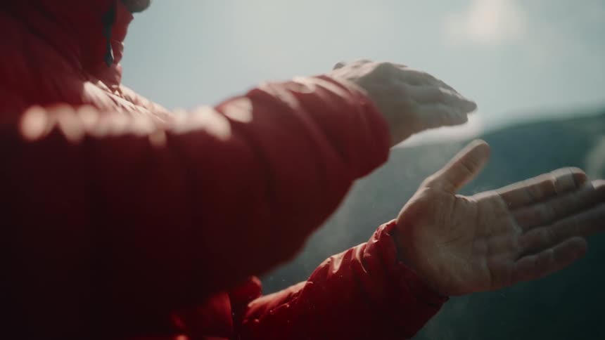 Cinematic slow motion close-up of a male rock climber clapping his hands together, creating a cloud of chalk dust in the bright sun