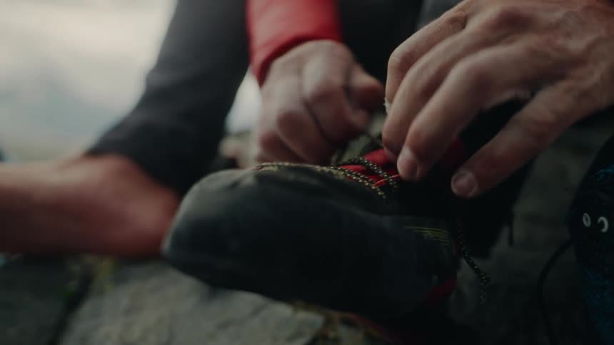 A mountain climber carefully ties his specialized climbing shoe in preparation for his ascent