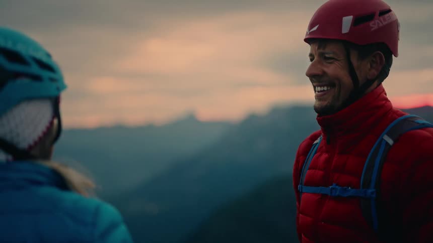 Two triumphant climbers celebrate with a slow-motion high-five on a mountain peak at sunset