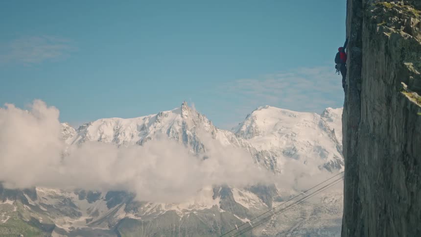 A rock climber scales a sheer cliff with the majestic snow-capped peaks of Mont Blanc in the background