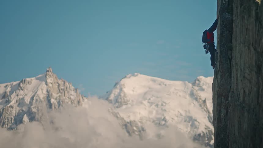 A lone climber scales a sheer rock face, dwarfed by the immense and majestic snow-covered mountains in the background