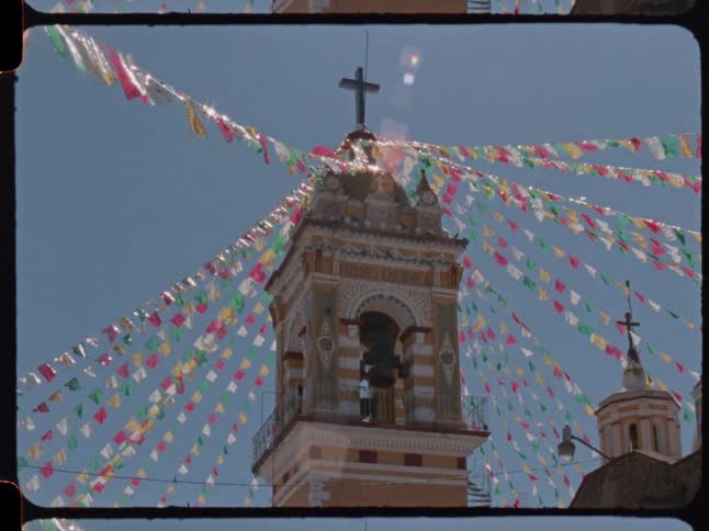 Vintage film captures colorful festival banners waving in the wind in front of a historic church bell tower