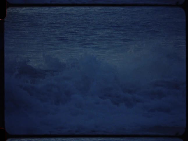Vintage Super 8 footage of a dark blue ocean wave building and breaking in slow motion
