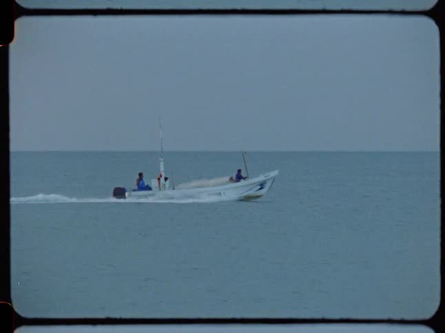 Two fishermen in a small motorboat cruise across the calm ocean on an overcast day, captured on vintage film