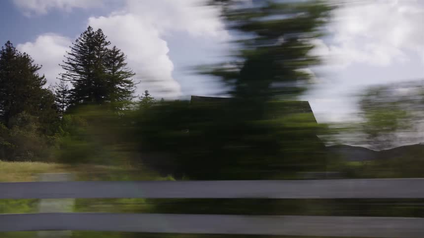 Passing by a classic red barn with a white fence while driving through the scenic countryside on a bright day
