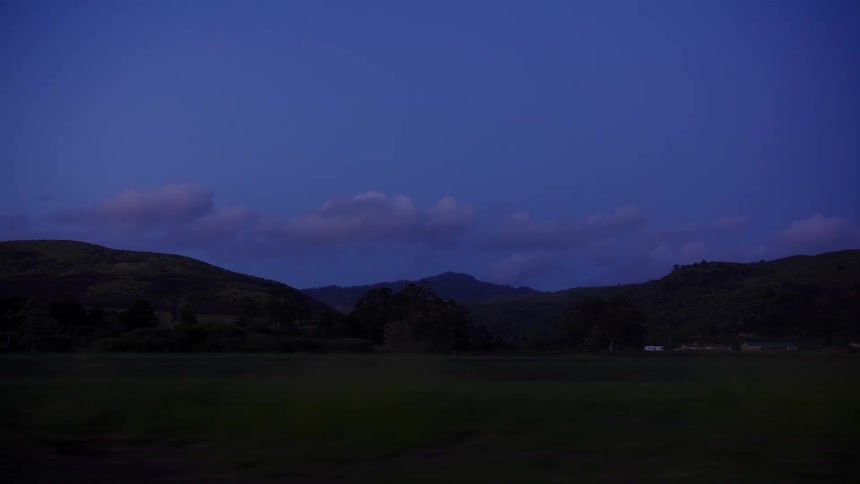A tranquil drive through the countryside at dusk, passing by dark fields and hills under a deep blue sky