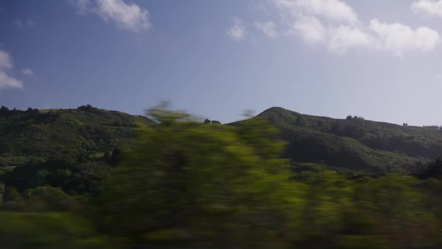 Passenger's point of view driving past beautiful green rolling hills in the countryside